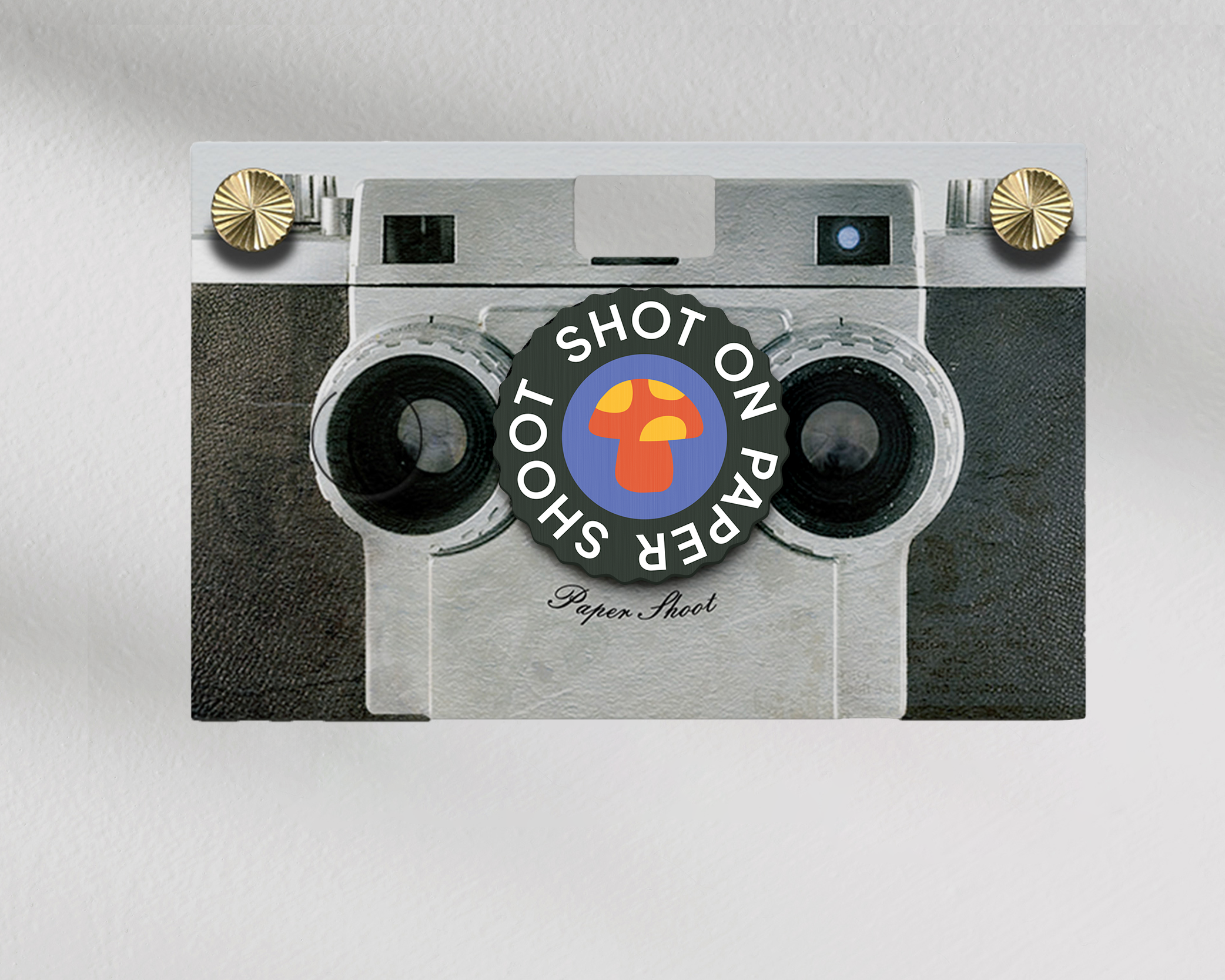 Shot on paper shoot text lens cover with center red and yellow mushroom graphic with grip groves on a paper shoot camera 