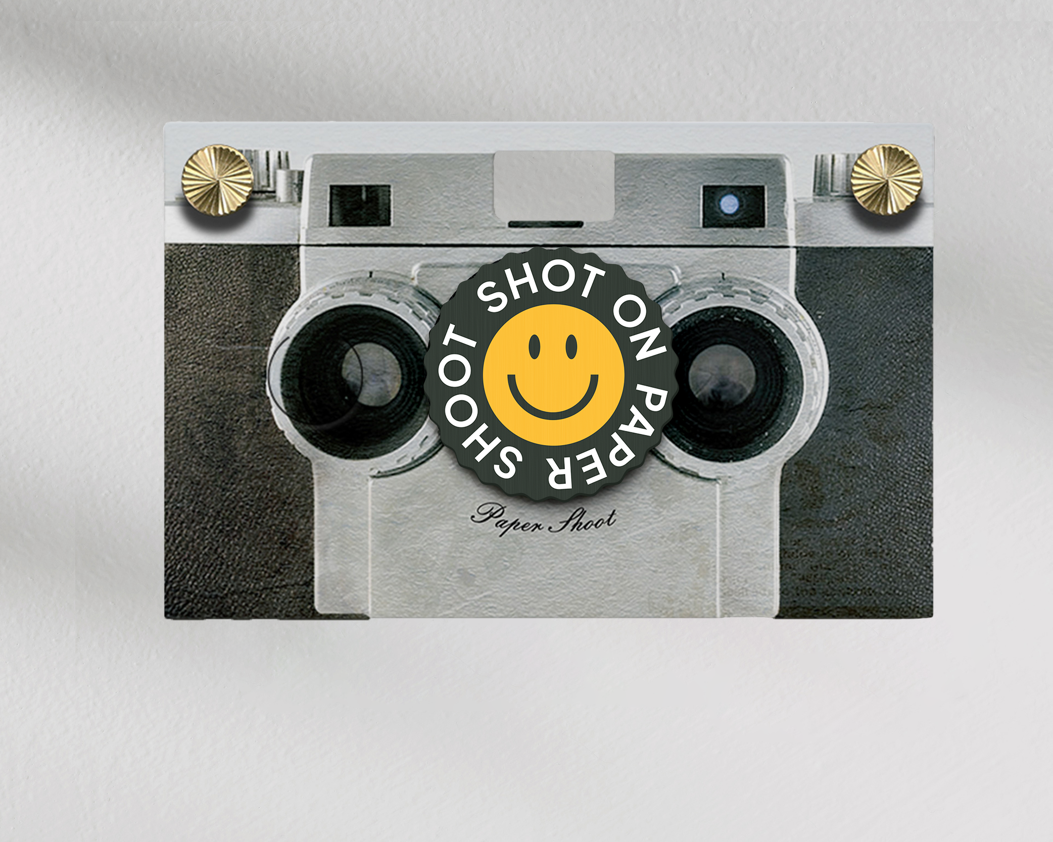 Shot on paper shoot text lens cover with yellow smiley face graphic with grip groves on a paper shoot camera 
