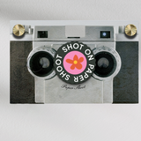 Shot on paper shoot text lens cover with red and yellow flower graphic with grip groves on a paper shoot camera 